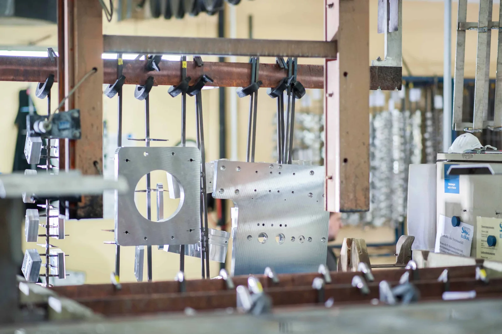 Gestell mit gefrästen Aluminiumplatten an der Eloxalanlage, rechts ein Schild mit S&W-Eloxal-Logo