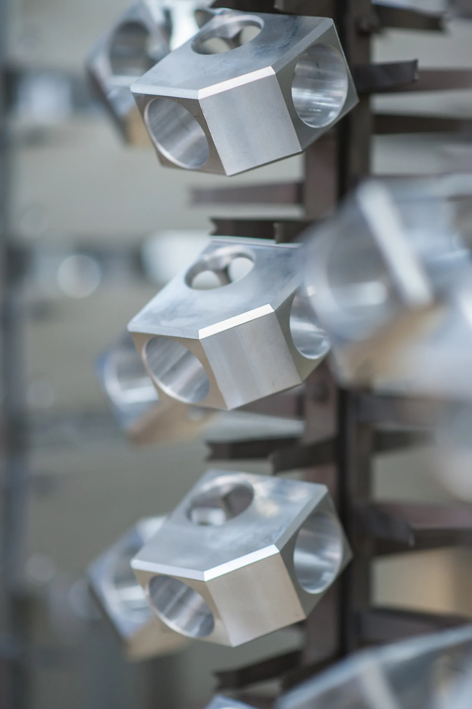Gefräste Aluminiumblöcke hängen an einem Gestell, nach hinten unscharf