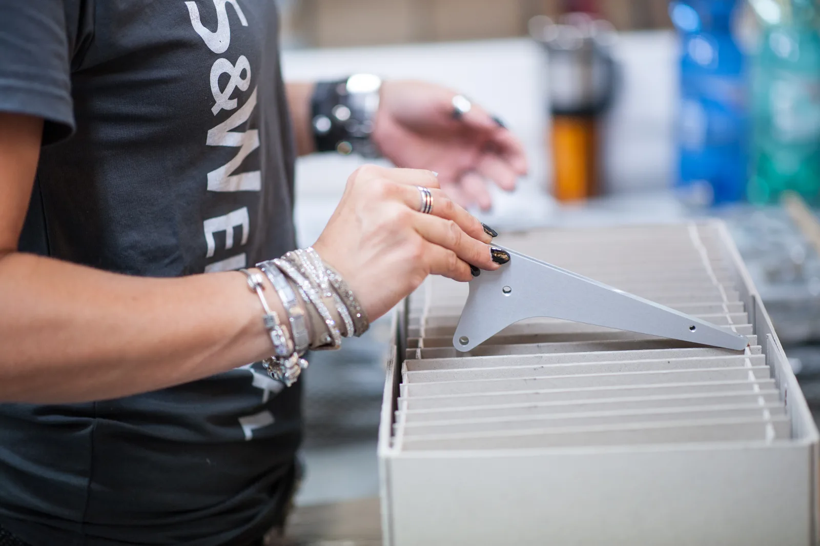 Hände sortieren eloxierte Aluminiumteile in einen Karton, im Hintergrund ein S&W-Shirt