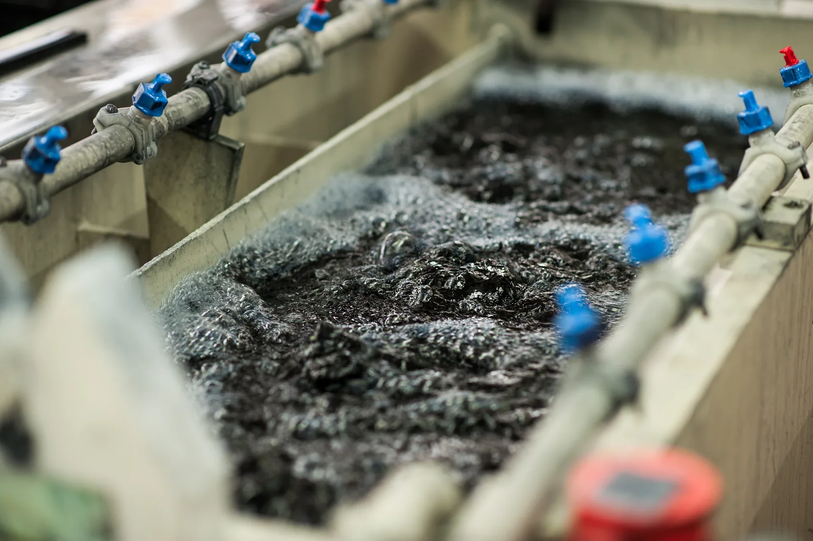 Becken der Eloxalanlage mit Schaum auf der Oberfläche, darüber eine Leitung mit blauen Düsen