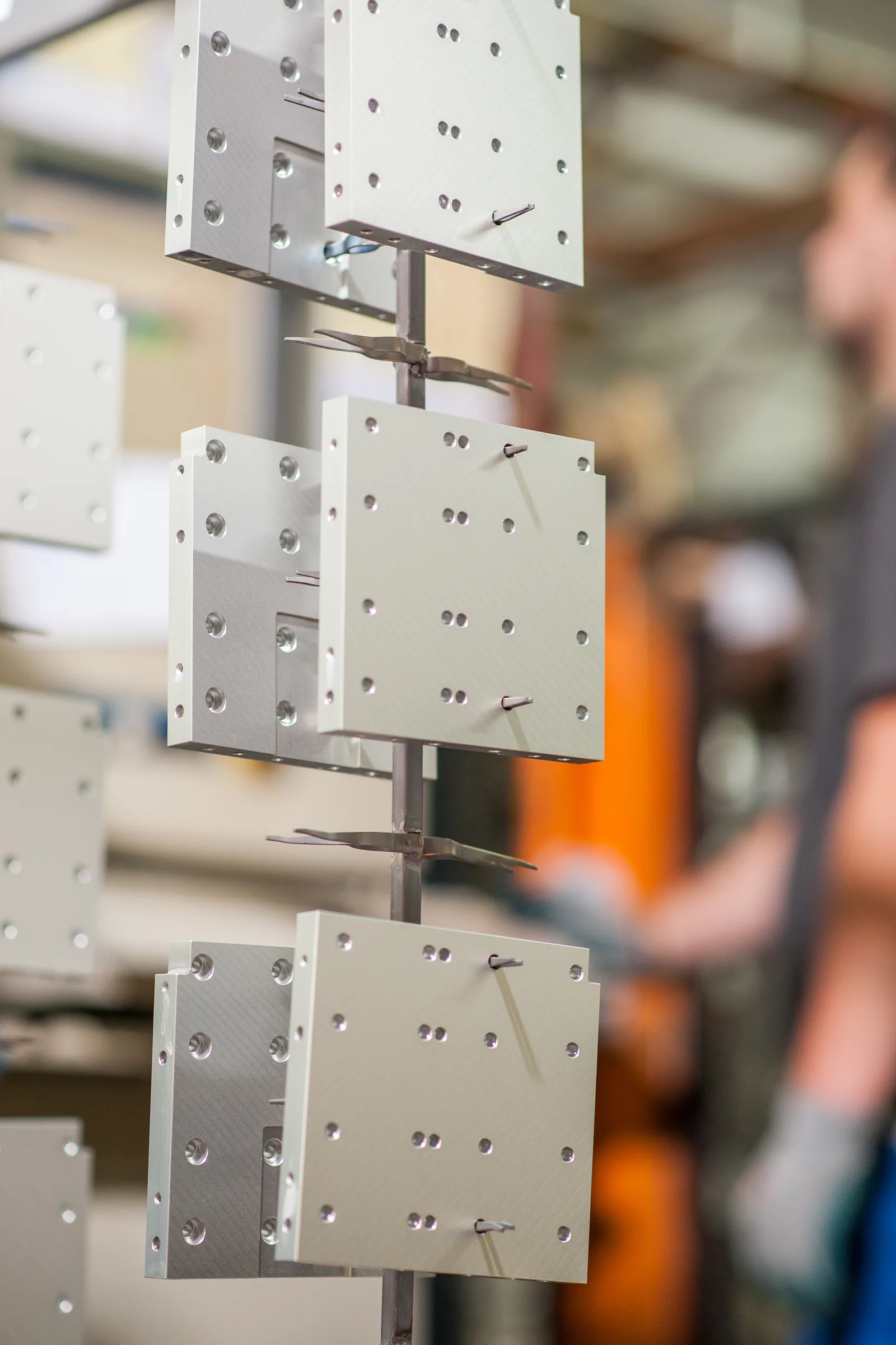 Helle Aluminiumplatten hängen an einem Gestell, dahinter unscharf ein Mitarbeiter